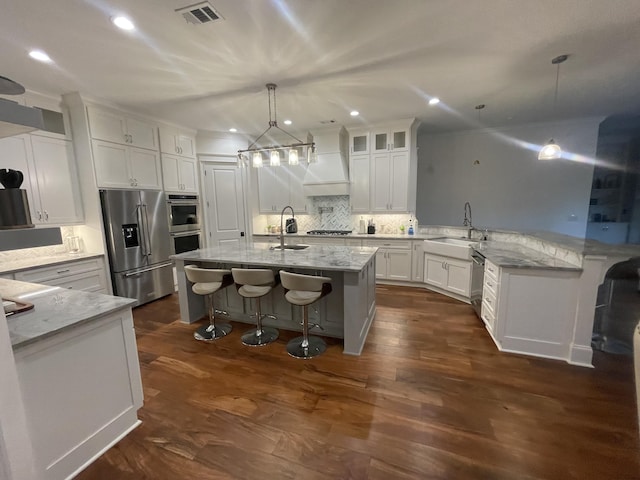 kitchen with backsplash, light stone counters, sink, a center island with sink, and white cabinets