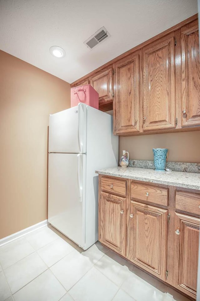 kitchen featuring white refrigerator, light tile patterned flooring, and light stone countertops