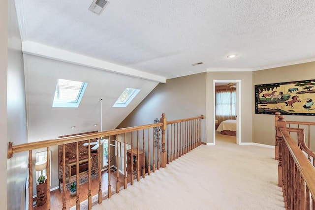 hallway featuring ornamental molding, vaulted ceiling with skylight, light carpet, and a textured ceiling