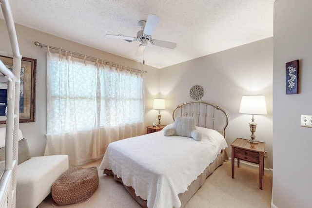 bedroom with ceiling fan, light carpet, multiple windows, and a textured ceiling