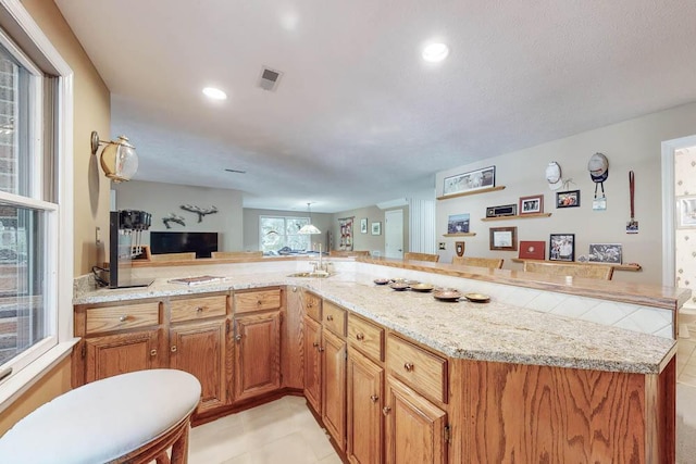 kitchen with light tile patterned floors, a kitchen breakfast bar, light stone countertops, and kitchen peninsula