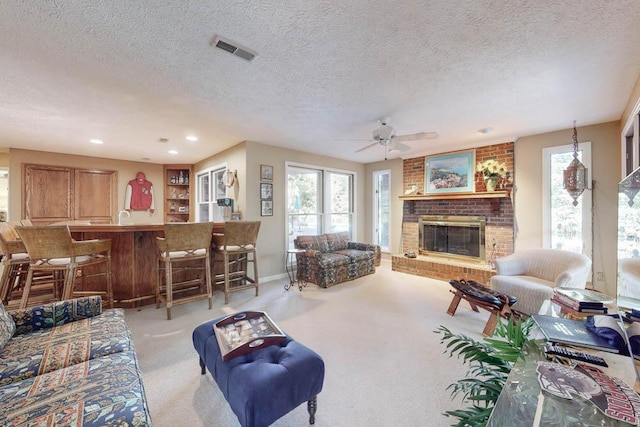 carpeted living room with a brick fireplace, a textured ceiling, and ceiling fan