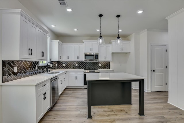 kitchen featuring sink, appliances with stainless steel finishes, white cabinetry, hanging light fixtures, and a kitchen island