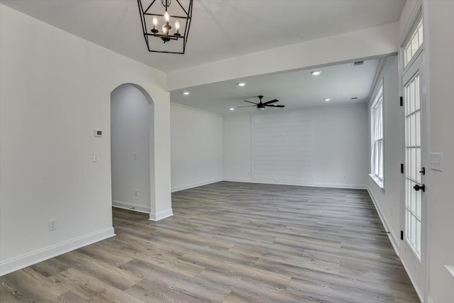 spare room with ceiling fan with notable chandelier and light wood-type flooring