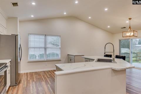 kitchen with white cabinets, sink, hanging light fixtures, light stone countertops, and an island with sink