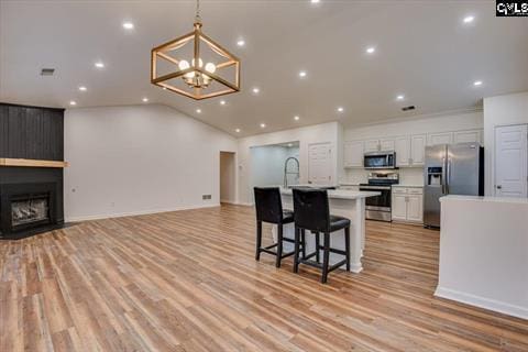 kitchen featuring a kitchen bar, appliances with stainless steel finishes, a fireplace, white cabinets, and an island with sink