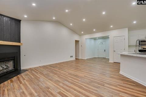 unfurnished living room with sink, a fireplace, lofted ceiling, and light hardwood / wood-style flooring