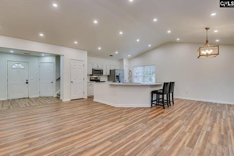 kitchen featuring appliances with stainless steel finishes, a large island with sink, decorative light fixtures, light hardwood / wood-style flooring, and white cabinetry