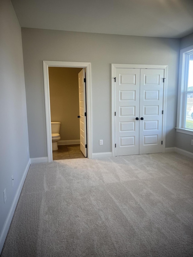 unfurnished bedroom with a closet, carpet flooring, baseboards, and ensuite bathroom