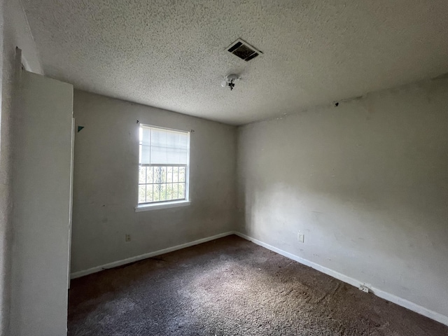 spare room with a textured ceiling, carpet flooring, visible vents, and baseboards