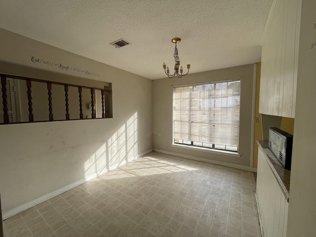 spare room with a notable chandelier, light floors, visible vents, a textured ceiling, and baseboards