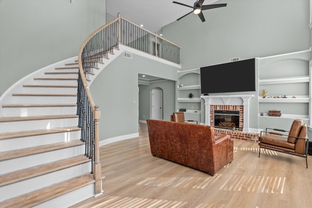 living room with hardwood / wood-style flooring, ceiling fan, a high ceiling, a brick fireplace, and built in shelves