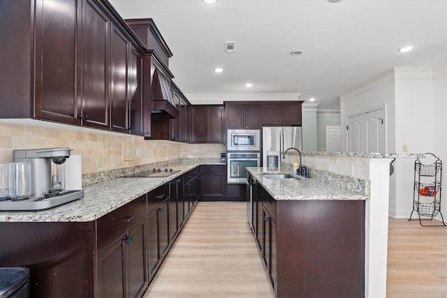 kitchen with appliances with stainless steel finishes, light hardwood / wood-style floors, sink, and a center island with sink