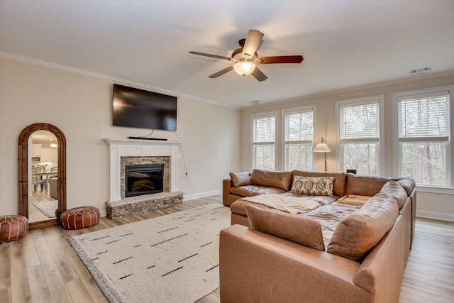 living room with a stone fireplace, ceiling fan, ornamental molding, and light hardwood / wood-style flooring