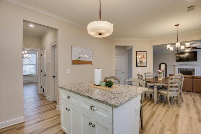 kitchen with light stone counters, light hardwood / wood-style flooring, decorative light fixtures, white cabinetry, and a stone fireplace