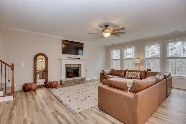 living room with crown molding, ceiling fan, light hardwood / wood-style flooring, and a stone fireplace