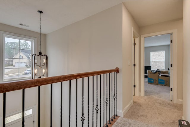 hallway with a notable chandelier, a wealth of natural light, and light carpet