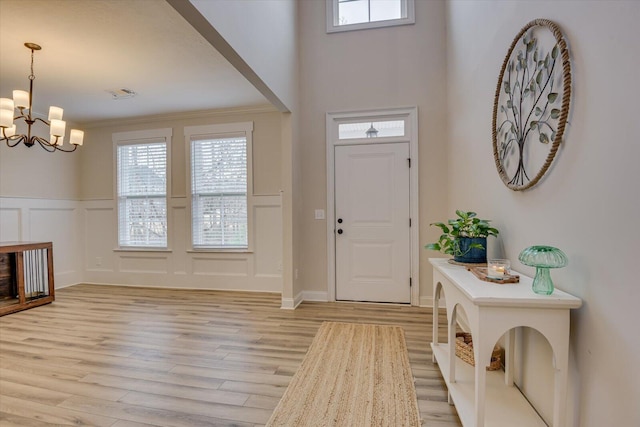 foyer featuring an inviting chandelier, light hardwood / wood-style floors, and crown molding