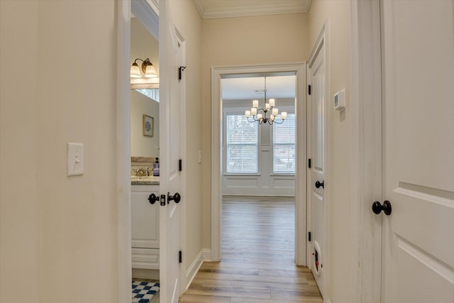 corridor featuring light wood-type flooring, an inviting chandelier, and ornamental molding