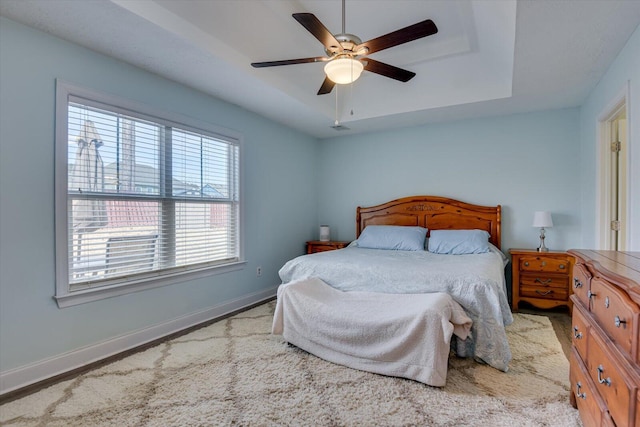 bedroom with ceiling fan, light hardwood / wood-style flooring, and a tray ceiling