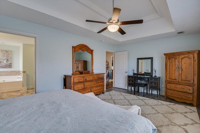 bedroom featuring ceiling fan, ensuite bathroom, and a tray ceiling