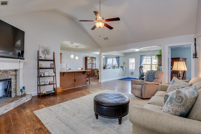 living room with ceiling fan, vaulted ceiling, a fireplace, and dark wood-type flooring