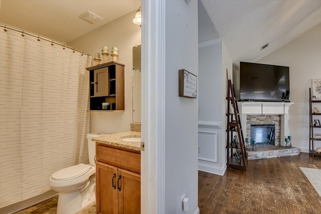 bathroom featuring lofted ceiling, vanity, a fireplace, toilet, and hardwood / wood-style flooring