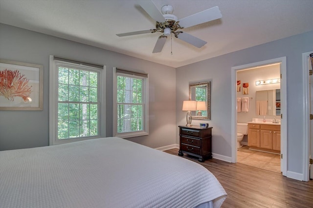 bedroom with light wood-type flooring, ceiling fan, and ensuite bath