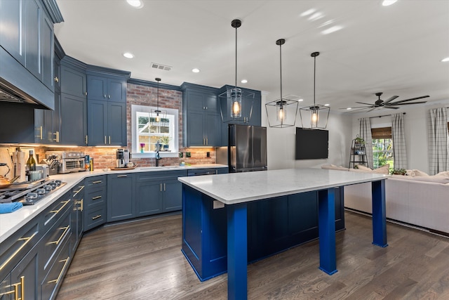 kitchen featuring black refrigerator, pendant lighting, a breakfast bar, a center island, and blue cabinetry