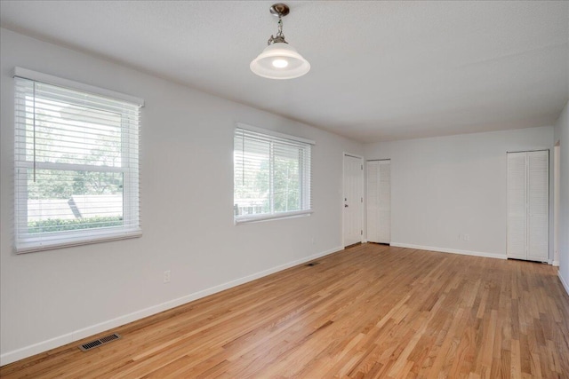 empty room with baseboards, visible vents, and light wood finished floors