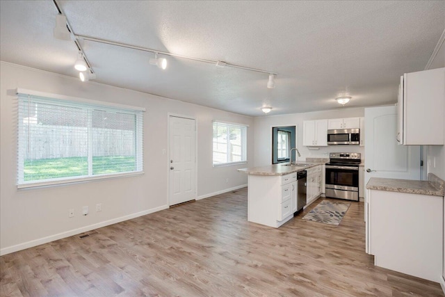 kitchen featuring track lighting, a peninsula, white cabinetry, a sink, and appliances with stainless steel finishes