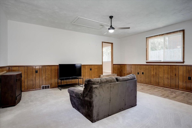 living area featuring wooden walls, wainscoting, a healthy amount of sunlight, and attic access