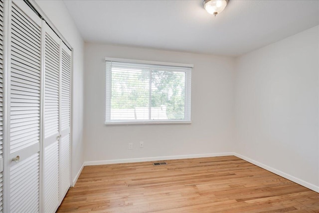unfurnished bedroom with baseboards, a closet, light wood finished floors, and visible vents