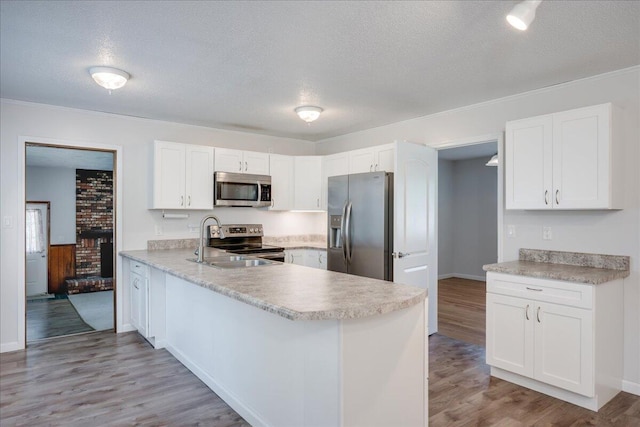 kitchen featuring a textured ceiling, a sink, a peninsula, stainless steel appliances, and white cabinetry