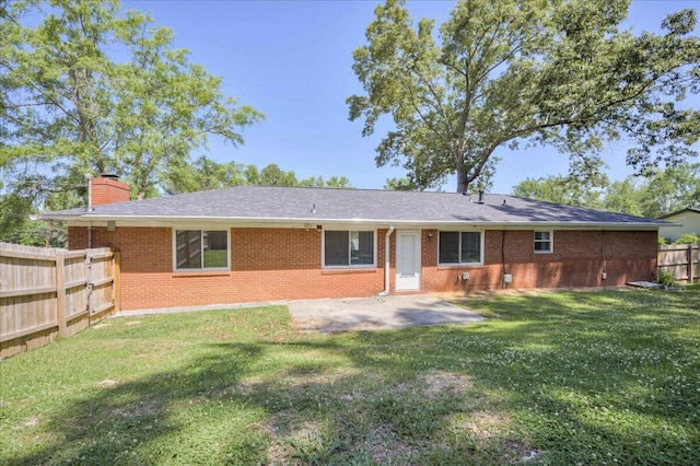back of house featuring a chimney, a lawn, brick siding, fence, and a patio