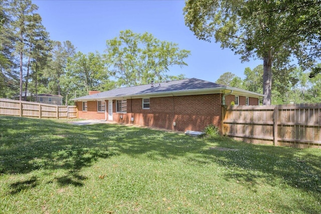 rear view of property featuring fence, a patio, a chimney, brick siding, and a yard