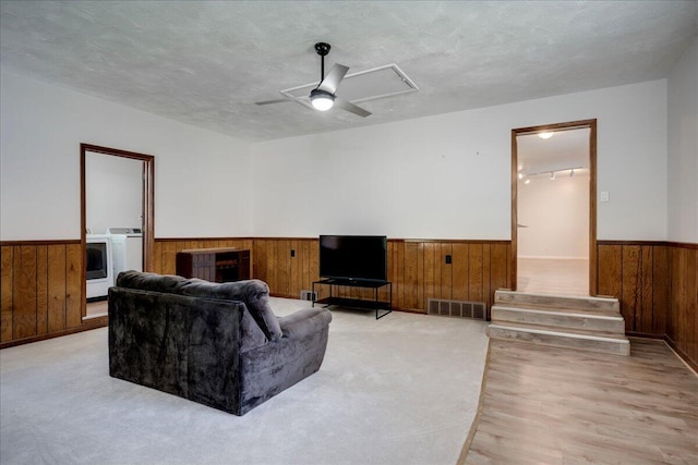 living room with wooden walls, ceiling fan, light wood-style flooring, a wainscoted wall, and visible vents