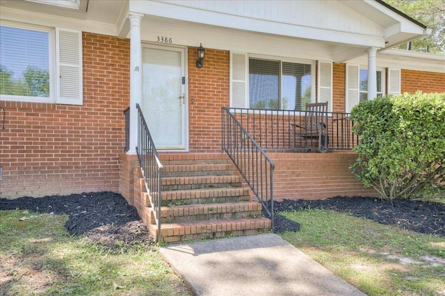 doorway to property featuring a porch and brick siding
