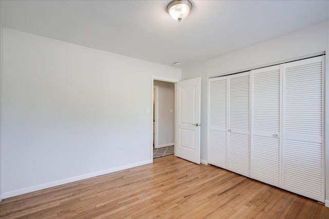 unfurnished bedroom featuring light wood-style floors, baseboards, and a closet