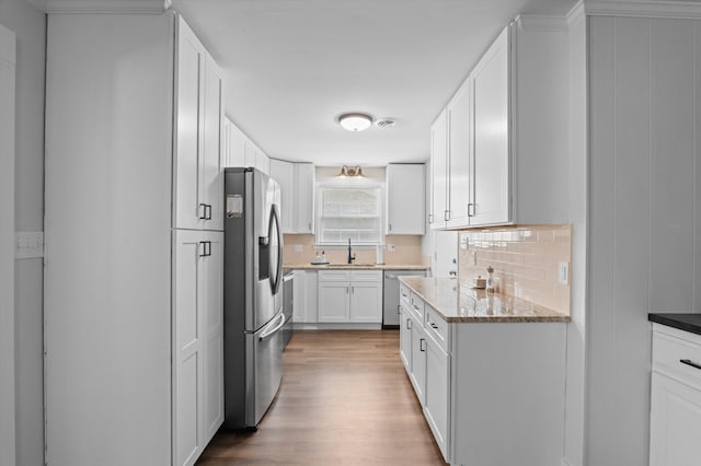 kitchen featuring tasteful backsplash, wood finished floors, appliances with stainless steel finishes, white cabinets, and a sink