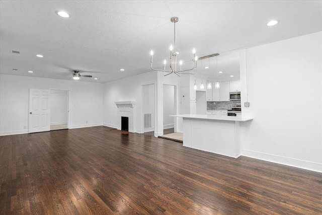 unfurnished living room featuring ceiling fan with notable chandelier, dark hardwood / wood-style floors, and a brick fireplace