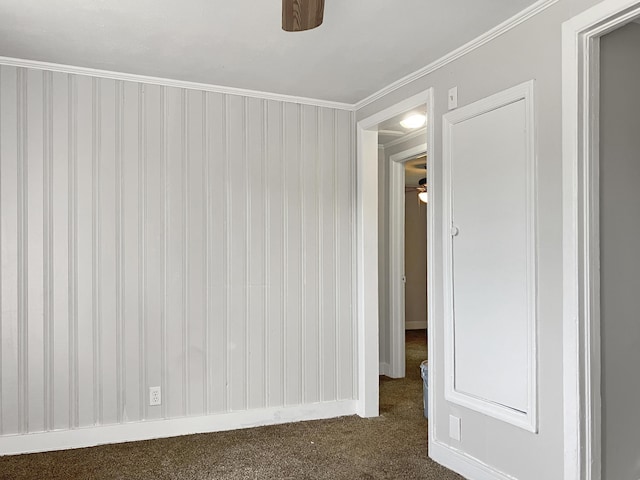 empty room with ceiling fan, dark colored carpet, crown molding, and baseboards