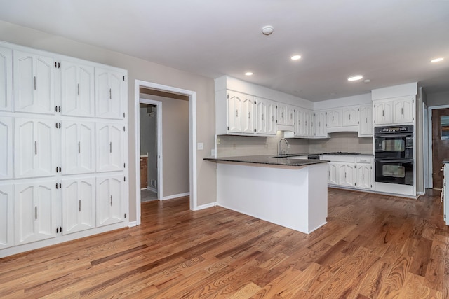 705 Woodgate Ct, Augusta, GA 30909 - kitchen featuring white cabinets, dark countertops, a peninsula, wood finished floors, and tasteful backsplash