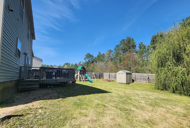 view of yard featuring a deck, a fenced backyard, a playground, a storage shed, and an outdoor structure