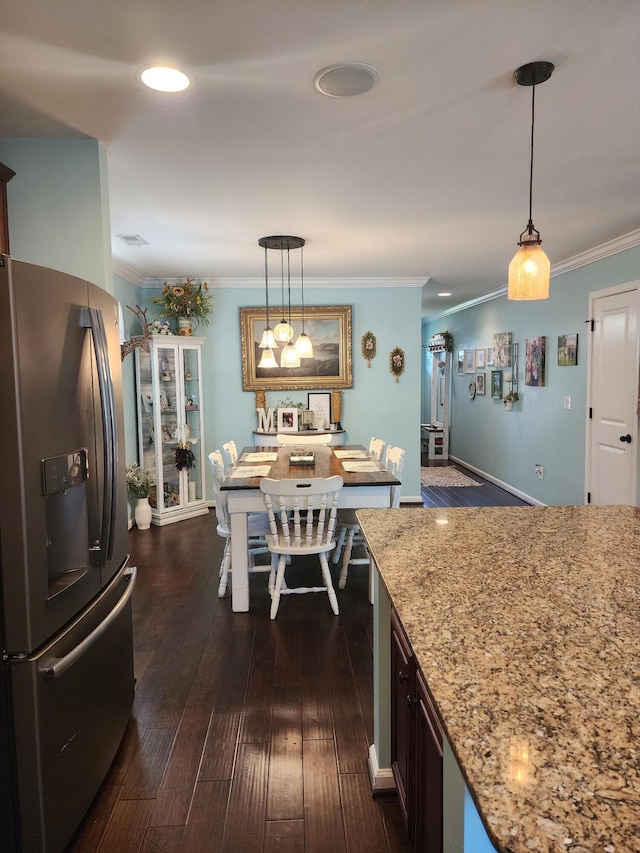 kitchen featuring light stone countertops, dark wood-style flooring, ornamental molding, hanging light fixtures, and stainless steel fridge