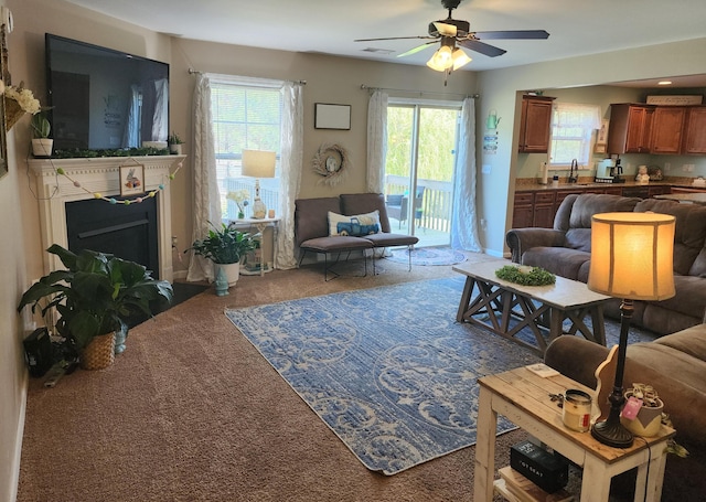 carpeted living area with a fireplace with flush hearth, a healthy amount of sunlight, visible vents, and ceiling fan