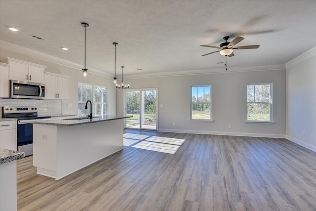 kitchen featuring decorative backsplash, ceiling fan with notable chandelier, stainless steel appliances, white cabinetry, and an island with sink