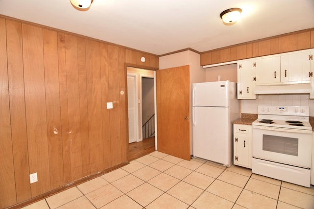 kitchen featuring light tile patterned flooring, wooden walls, under cabinet range hood, white appliances, and white cabinetry