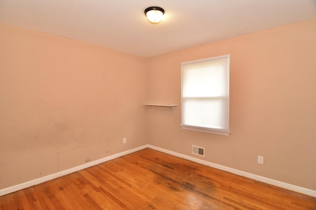 empty room with wood finished floors, visible vents, and baseboards