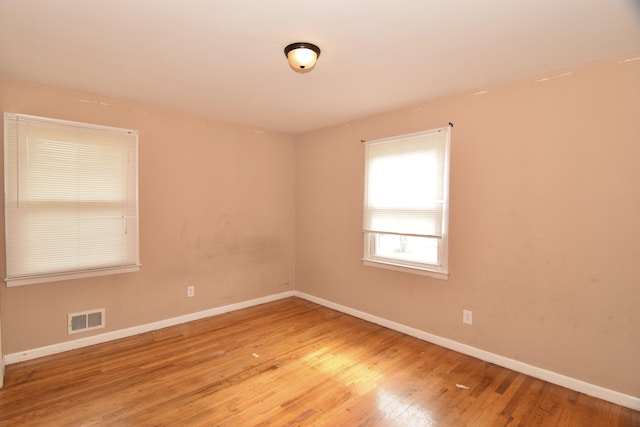 spare room with baseboards, visible vents, and wood finished floors